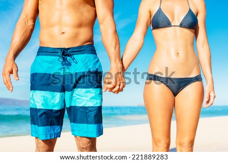 Attractive Fit Couple on the Beach in Swimwear Holding Hands