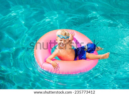 Young Kid Having Fun in the Swimming Pool On Inner Tube Raft. Summer Vacation Fun.