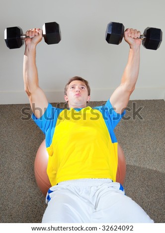 Athletic Male Lifting Weights in Gym Sitting On Medicine Ball