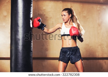 Beautiful Fitness Woman with the Red Boxing Gloves. Attractive Female Boxer Training Punching a Heavy Bag in the Gym.