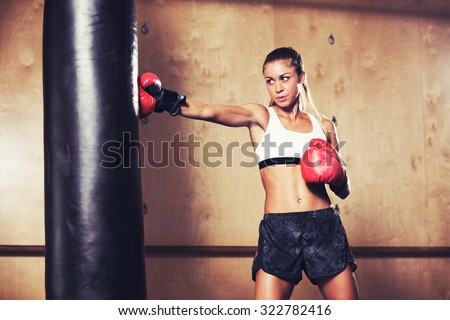 Beautiful Fitness Woman with the Red Boxing Gloves. Attractive Female Boxer Training Punching a Heavy Bag in the Gym.