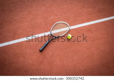 Tennis racket near a yellow ball on a brick red court