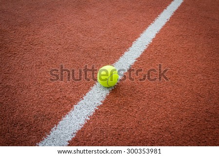 Yellow tennis ball on the white marking line of a brick red court