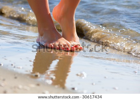 Pair of beautiful feet dancing on a beach of the  blue sea