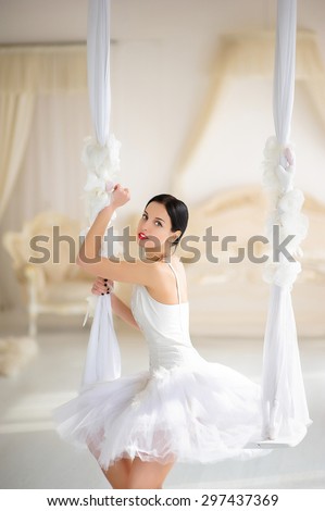 Beauty brunette ballerina on a swing in room, with ballet skirt and corset
