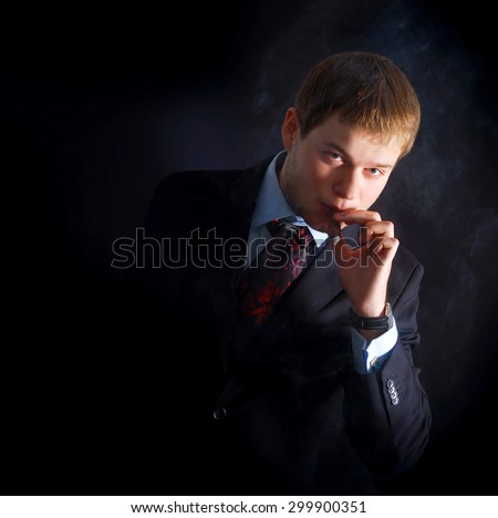 The man smoke a cigar. lots of smoke. A dark background