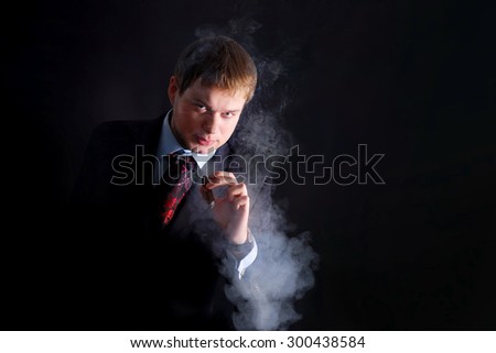 The man in suit smoke a cigar, lots of smoke. A dark background. Looks at us