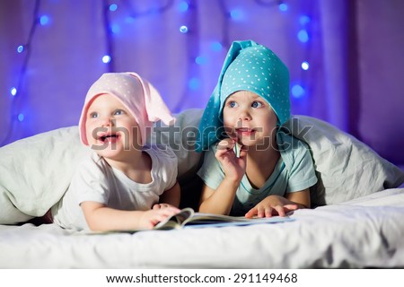 little girl and little boy in a cap to read a book in the spa konun christmas, looking away and smiling