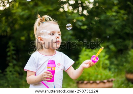 little blonde girl inflates soap bubbles on a summer day outdoors