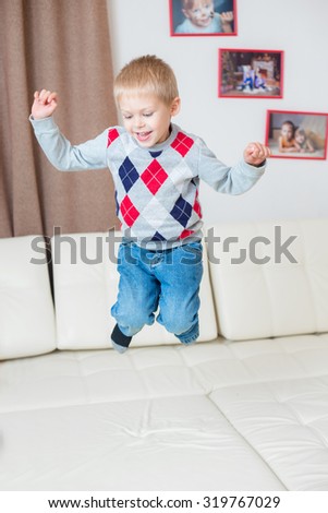 little blond boy jumping on a white leather couch