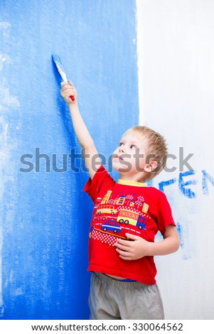 Cute blue-eyed blond pretty boy of five years in the red t-shirt makes repair paints the wall in blue paint brush
