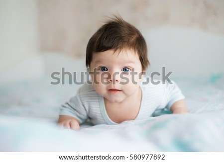baby, newborn baby cute blue-eyed, dark hair, baby 2 months in a blue body lying on his stomach