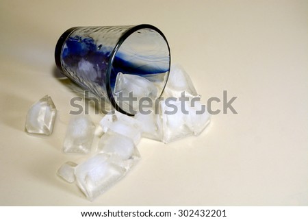 Ice cubes spilling out of topped over blue and clear glass