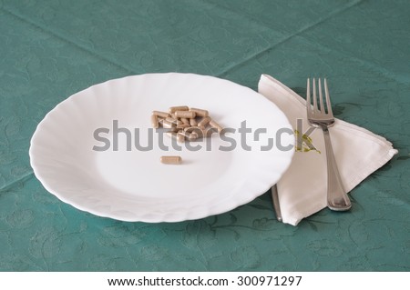 dietetic food, pills on white plate with cutlery and napkin on green tablecloth.\
emphasizing the idea of weight loss diet or healthy