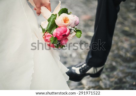Beautiful bouquet in hands of the bride in a white dress and the groom is seen shoe