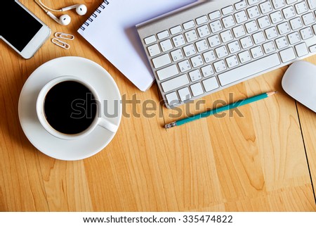Office wood table with keyboard notepad mouse earphone smart phone and coffee cup . Top view