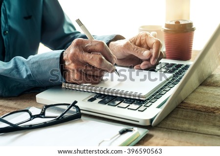 old man hand writing with a pen in a notebook,Handwriting  on office wood table with laptop computer