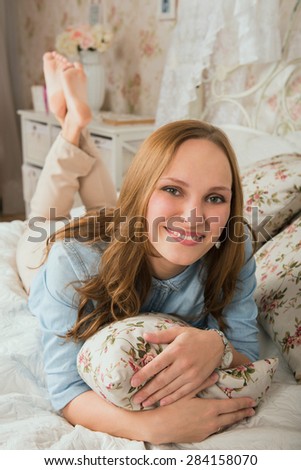 Happy blond woman lying in bed holding pillow and smiling. Bedroom in romantic, provance style