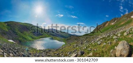 Bright sunny day on a mountain lake. Panorama with sun beams and blue clear sky.