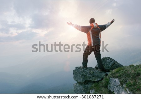 Happy man standing on the cliff of mountain with raised hands to the sun.  Hiker celebrating success.
