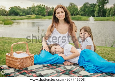 Mother with young daughters having picnic. Family in the same clothes near the lake
