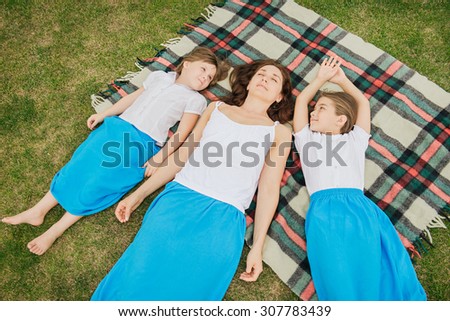 Top view photo of family relaxing on blanket on the nature. Daughters have the same clothes as mother and look at the mother