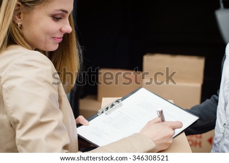 Beautiful woman receives package from courier. Close view of a customer signing delivery note
