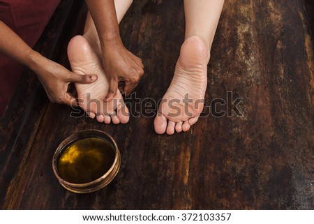 Ayurveda foot massage with oil on the wooden table in traditional style made by asian women. Top view.