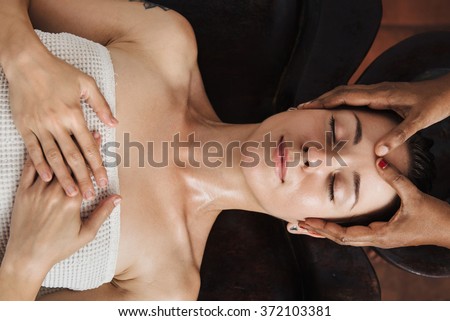 Ayurveda face massage with oil on the wooden table in traditional style made by asian women. Top view