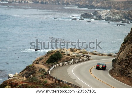 Photo of black sports car driving around a bend with a scenic ocean view in the back ground