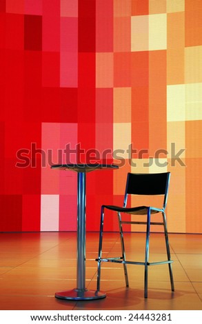 single chair and small table in front of a funky multiple-colored LCD screen