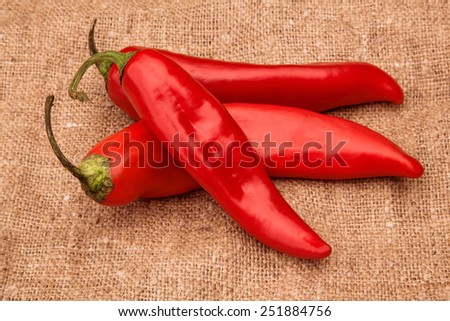 Three red pepper on sackcloth. Still-life - the top view.
