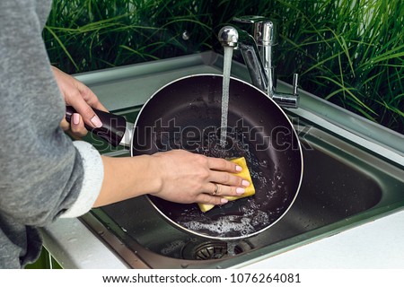 Female hand washing frying pan close up under running water, Young housewife woman washing griddle in a kitchen sink with a yellow sponge, Hand cleaning, manually, by hand, housework dishwasher,