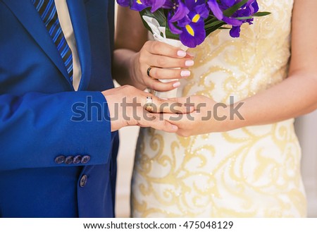 Beauty bride and handsome groom are wearing rings each other. Wedding couple on the marriage ceremony. Bride and groom\'s hands with wedding rings, Hands with wedding rings and fower bouquet