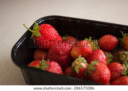 Fresh strawberries in black supermarket plastic tray of packaging on the marble table; Healthy low fat food for diet or sweet dessert from farmers market
