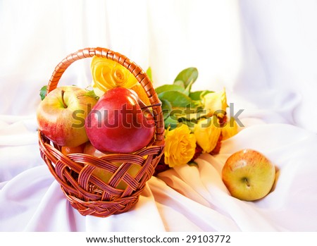 Apples in a basket and roses. Sharpness on a basket with apples, apple outside and roses out of sharpness