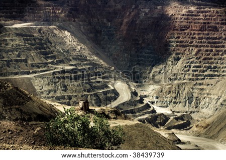 Open pit mine with a single lonely tree and rusty water tank  in the foreground