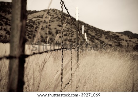 Abstract, grainy, old style sepia barbed wire fence in grassland with hills in the background