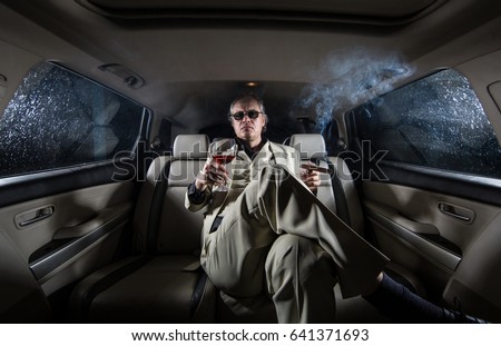 A rich man in a white suit and a cigar with a glass of wine in the car, a limousine