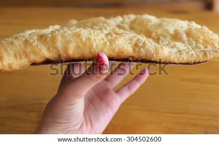 The girl is holding a big, juicy, delicious, fried, golden cheburek.
