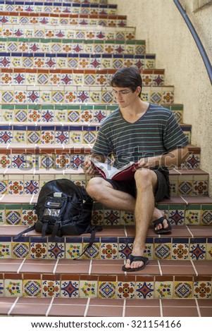 Attractive male student studying with textbooks on Spanish style tile steps, looking serious