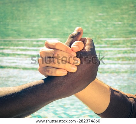 Black and white human hands in peaceful handshake representing friendship and respect - Arm wrestling together against racism - Vintage filtered look