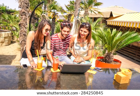 Group of happy best friends using laptop computer at beach bar restaurant - Spring break summer concept with young people having fun together with internet connection - Warm sunny afternoon color tone