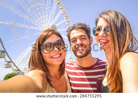 Best happy friends  with mobile taking selfie at ferris wheel - Three students at luna park - Concept of friendship and fun with new trend and technology - Young people enjoy with modern smartphone