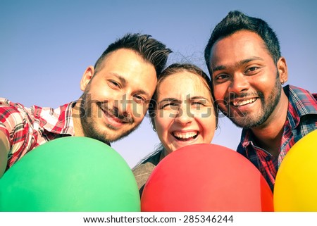 Multiracial group of young best friends taking selfie with mobile smart phone - Three happy smiling students have fun with modern smartphone and colorful balloons -Concept of multiethnic friendship