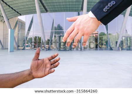 Hand of young american businessman reach out black refugee arm - Humanitarian aid against racism - Black and white hands reaching - Concept of European community aid to african people escape from war