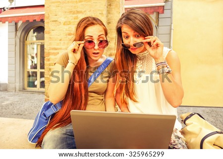 Young women with computer laptop looking surprised - Best friends using pc online outdoors in old town center - Autumn tourist females having astonished facial expression - Modern concept of leisure