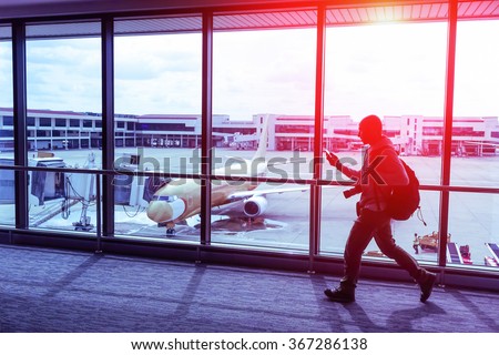 Silhouette of walking  man with smartphone at generic international airport terminal -  Traveling person with bag inside gate ready to flight - Tilted composition with modified paintings on the plane