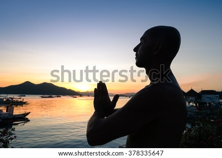 Silhouette of man doing yoga exercises at sunset on the terrace overlooking the ocean - Young person during meditation training - Concept of relaxation with twilight colors and orange filter look