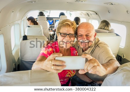 Senior happy couple taking selfie with mobile phone on board of plane -  Smiling retired people having fun flying from Coron to Borakay by airplane - Concept of elderly happiness on world wide travel